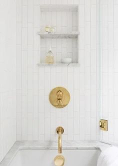 a bathroom with white tile and gold fixtures in the bathtub, along with shelving on the wall