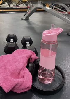 a pink towel is next to a water bottle and dumbbells on a gym floor