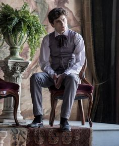 a young man sitting on top of a chair next to a plant in a vase