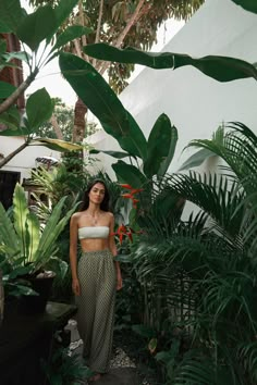 a woman is standing in the middle of some tropical plants and trees with her head turned to the side