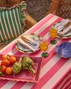 a table set with plates, glasses and oranges on top of pink and white striped cloth