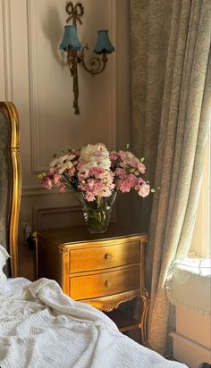 a vase with flowers sitting on top of a wooden table next to a bed in a room