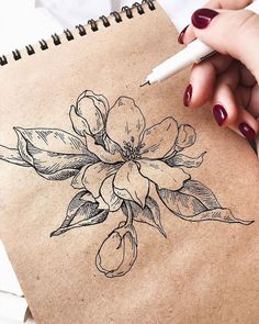 a woman's hand holding a pen and drawing flowers on a piece of brown paper