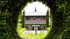 the house is surrounded by green bushes and trees, as seen through a circular hole in the hedge