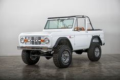 an old white truck is parked in a room with concrete flooring and large tires