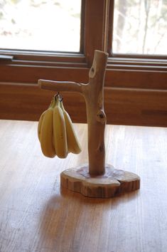 two bananas hanging from a tree branch on a wooden table in front of a window