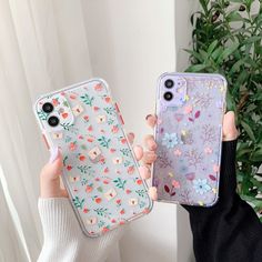 two women holding up their phone cases with flowers on them, one is clear and the other is blue