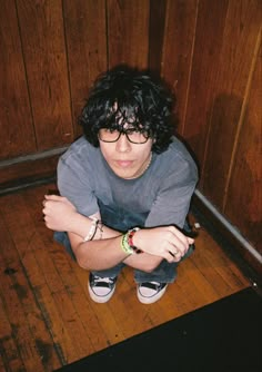 a young man sitting on the floor with his arms crossed and looking at the camera