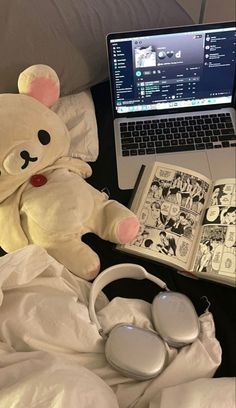 a teddy bear sitting on top of a bed next to a laptop computer and headphones