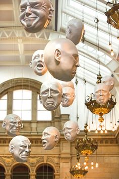 many faces are hanging from the ceiling in a large room with chandeliers and windows