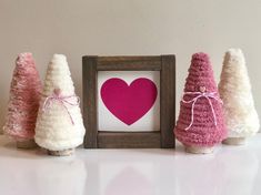 three small crocheted trees in front of a frame with a heart on it