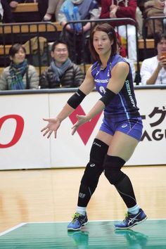 a woman in blue uniform playing volleyball on court with crowd watching from bleachers