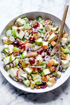 a white bowl filled with apples, celery, walnuts and cranberries