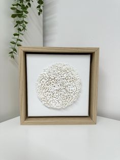 a white and brown framed artwork on a table next to a potted green plant