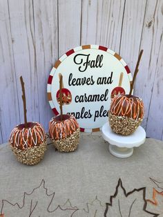 three caramel apples sitting on top of a white plate next to a sign that says fall leaves and caramel cakes pies