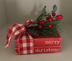 a stack of christmas books with holly and pine cones on top, wrapped in red plaid ribbon