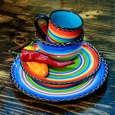 a stack of multicolored plates and cups on a wooden table with a chili pepper