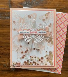 a close up of a card on a wooden surface with buttons and paper butterflies in the background