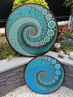 two blue plates sitting next to each other on top of a stone wall in front of a planter