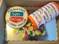 a decorated birthday cake in a box with writing on the side and an orange tube