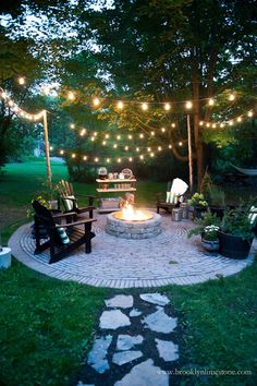 an outdoor fire pit surrounded by string lights and potted plants in the back yard