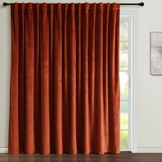 an orange curtain hanging on the side of a window in front of a white wall