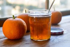 an orange sitting next to a jar of liquid on top of a wooden table with two oranges in the background