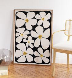 a white and black flowered painting next to a chair in a room with hard wood flooring