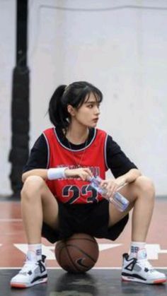 a young woman sitting on top of a basketball court holding a bat and wearing sneakers