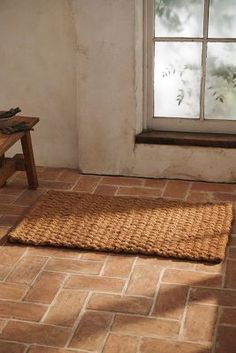 an empty room with a bench, window and rug on the floor in front of it