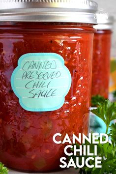 canned chili sauce in a glass jar with a blue sticker on the lid and green herbs around it