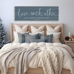 a bed with pillows and blankets in front of a wooden sign that says love each other as i have loved you