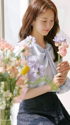 a woman sitting on a window sill with flowers in her hand and looking down