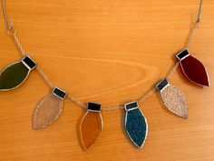 a necklace with four different colored leaves hanging from it's sides on a wooden surface