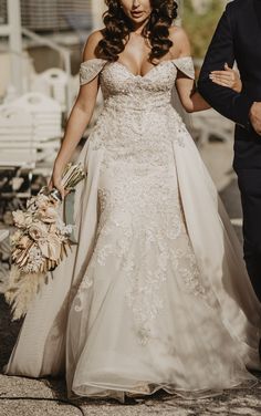 a woman in a wedding dress walking down the street next to a man wearing a suit