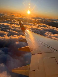 the wing of an airplane as it flies above the clouds at sunrise or sunset time