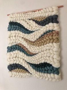 a wall hanging made out of different colored yarns on a white wall with a wooden stick