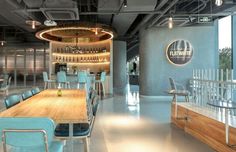 an empty restaurant with blue chairs and wooden tables in front of the bar area that has a circular light fixture hanging from the ceiling