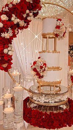 a three tiered wedding cake with red and white flowers on the top, surrounded by candles