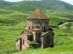 an old building in the middle of a green field with hills in the background and trees on both sides