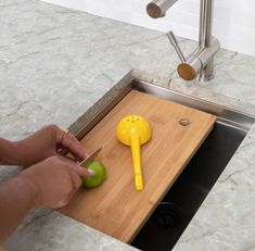 a person cutting an apple with a knife on a cutting board in front of a sink