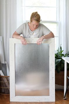 a woman is holding up a metal sheet in front of a window