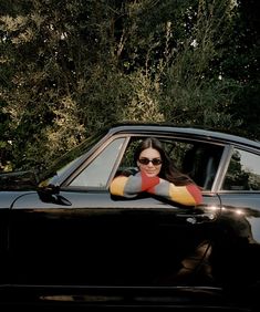 a woman sitting in the driver's seat of a black car with her arms crossed