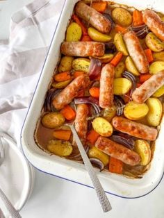 a casserole dish with sausages, potatoes and carrots in it on a table