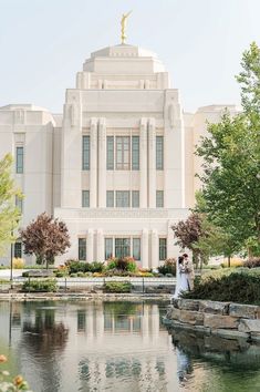 a bride and groom standing in front of a large white building with a pond on the side