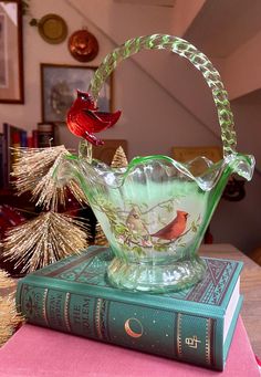 a glass basket sitting on top of a book next to a red bird figurine