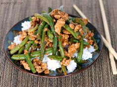 a plate with green beans, rice and meat on it next to chopsticks