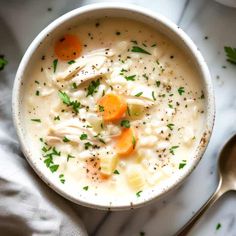 a bowl of chicken and dumpling soup with a spoon next to it on a marble surface