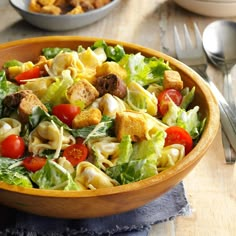 a wooden bowl filled with salad next to silverware