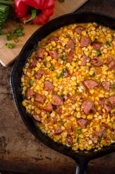 a skillet filled with corn and sausage on top of a wooden cutting board next to vegetables